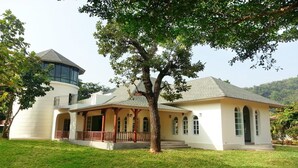 A two-story house with a large tree in front, a tower-like structure on the left, and a covered porch with columns. - GRANMONTE Wine Cottage (Pak Chong)