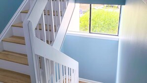 Eine Treppe mit weißen Geländern und Holzstufen, die zu einem Raum mit einem Fenster mit Blick auf Grünanlagen führt.