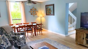 Ein Wohnzimmer mit Sofa, Couchtisch, Esstisch mit Stühlen, Fernseher und Treppe.