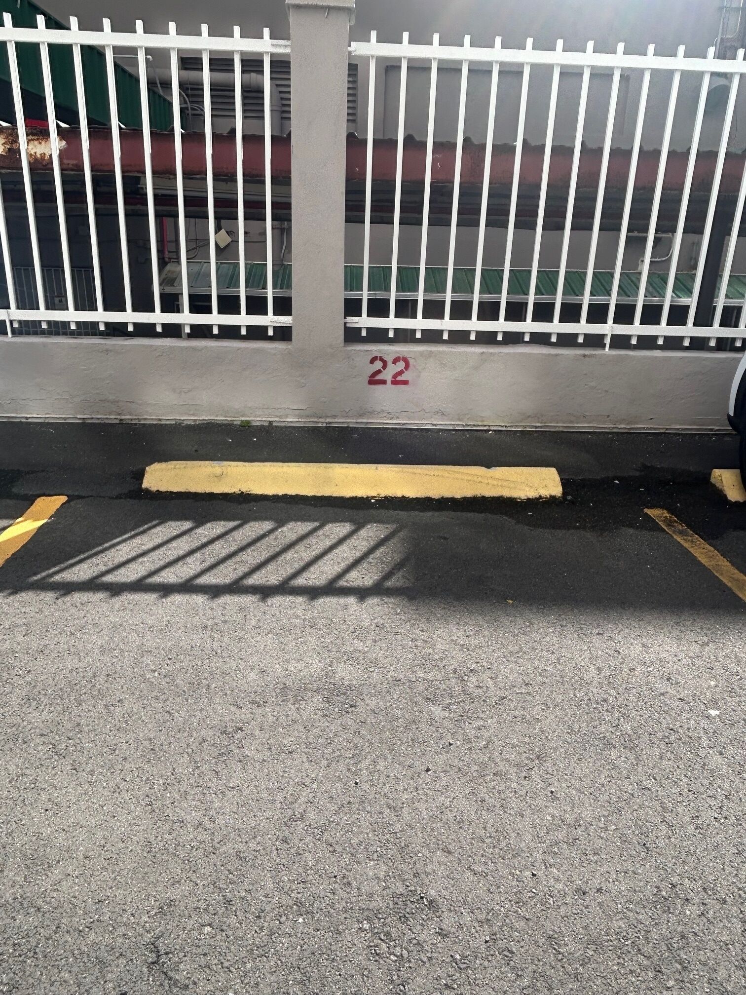 A parking area with a white metal fence, a yellow line, and the number 22 painted on the wall.