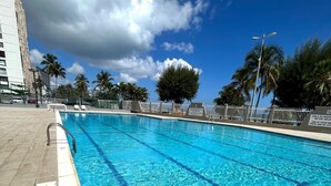 Ein Swimmingpool mit klarem, blauem Wasser, umgeben von einer gefliesten Liegefläche, Palmen und einem Gebäude im Hintergrund.