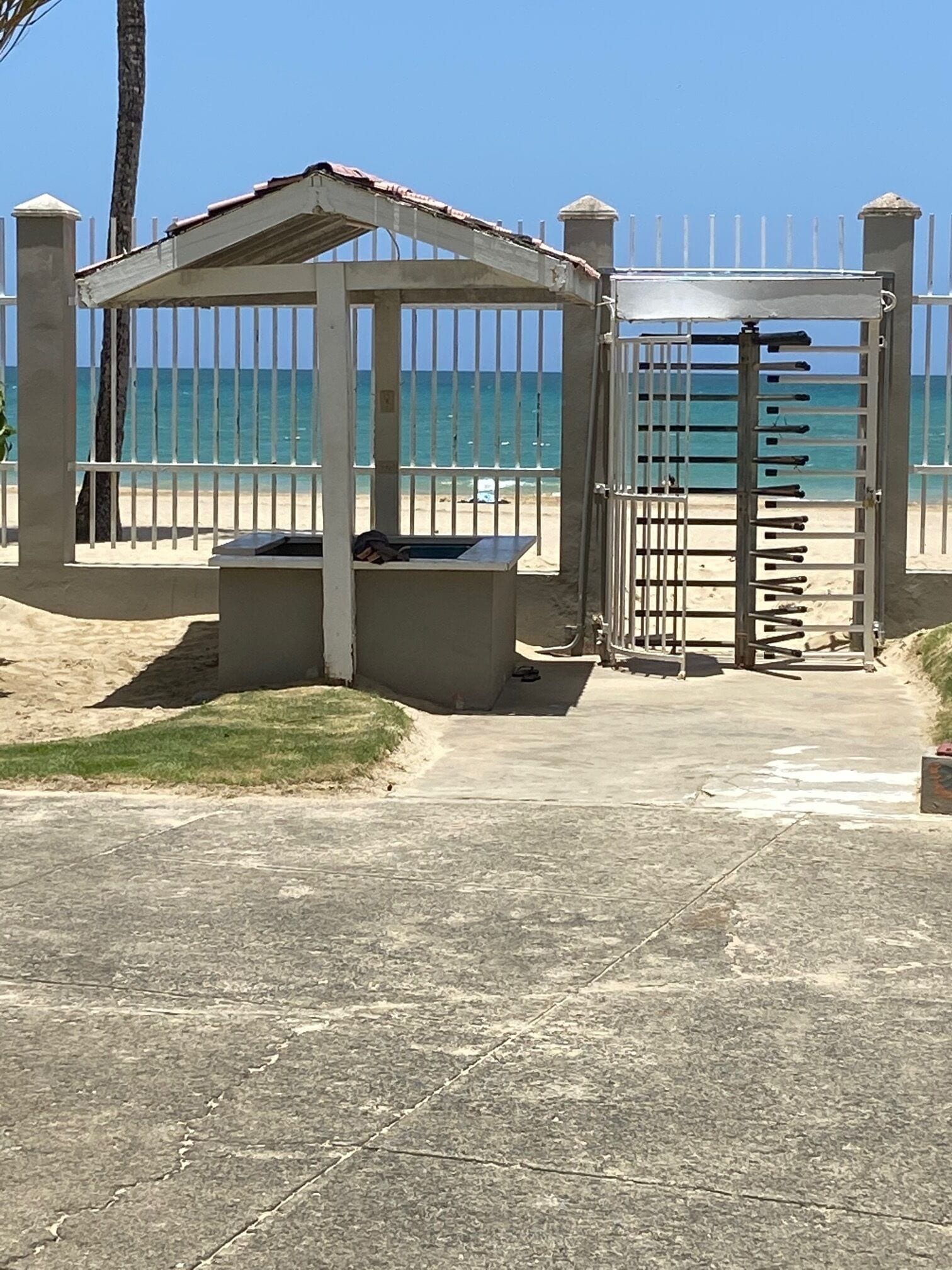 A gated beach area with a concrete walkway, a covered seating area, and a view of the ocean.