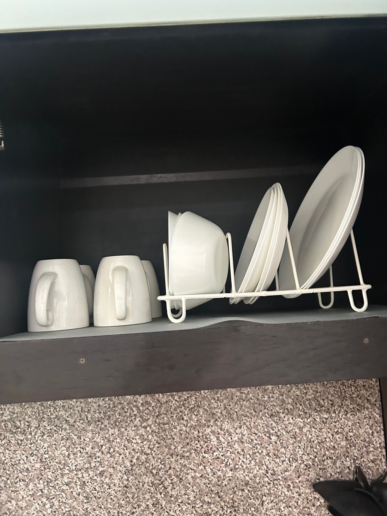 Una estantería en la cocina con tazas blancas, una tetera y un escurreplatos.