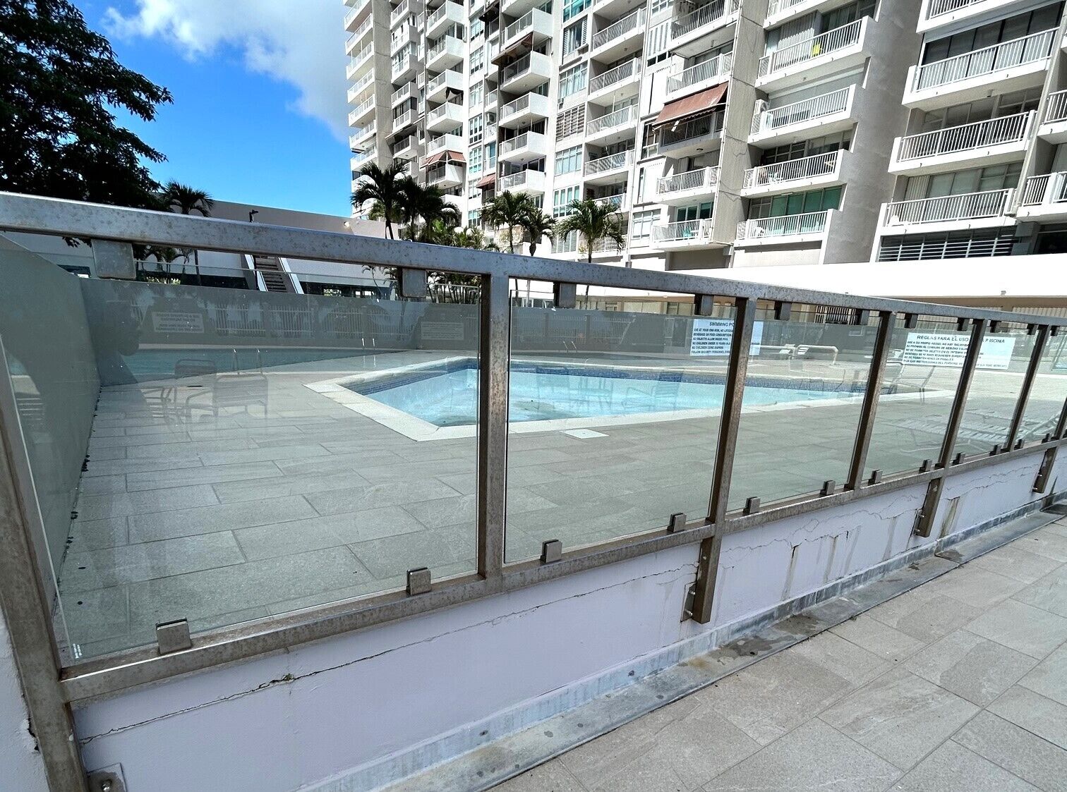 Una piscina con barriera in vetro, circondata da un grattacielo con balconi.
