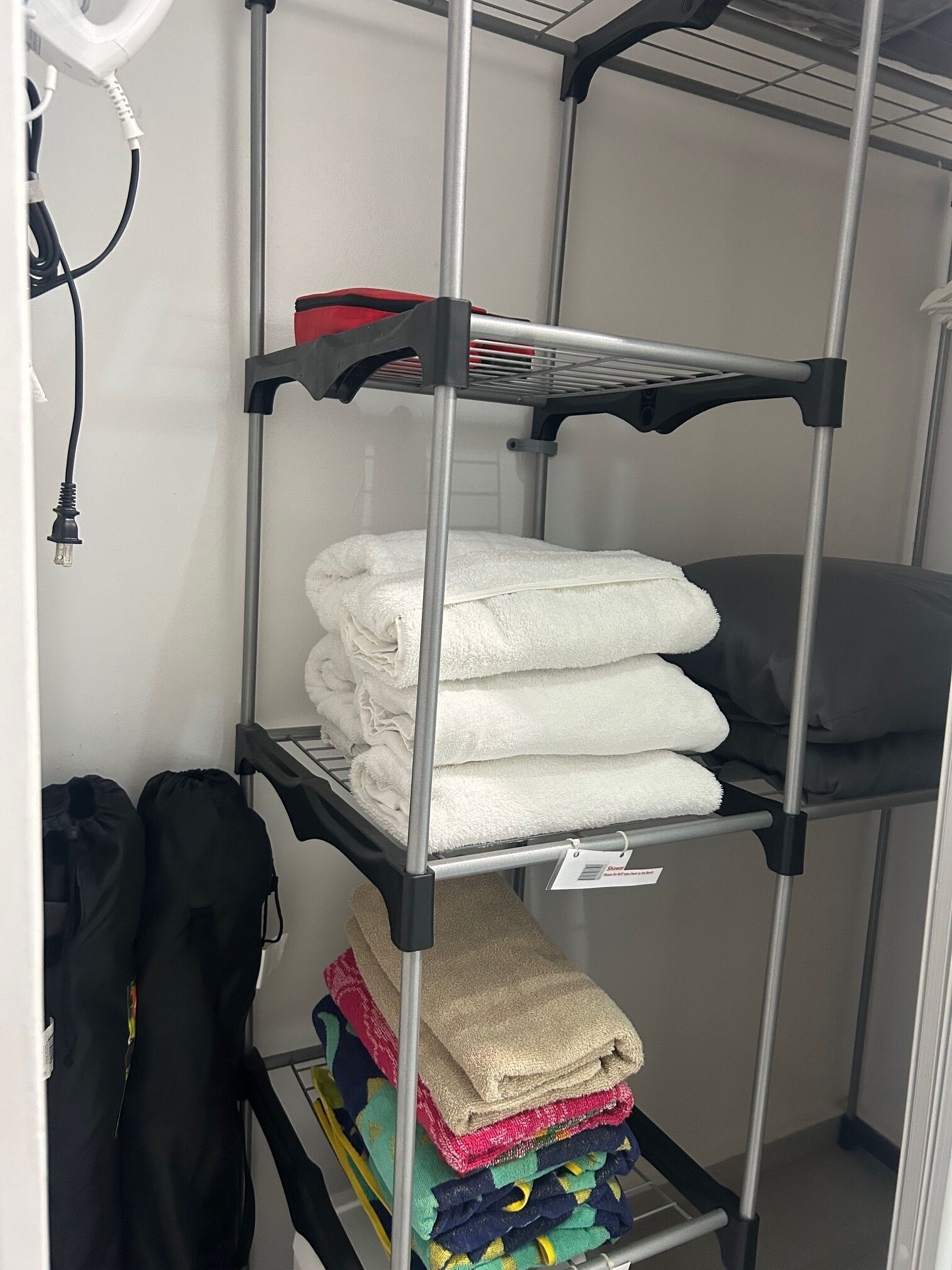Une étagère en métal avec des serviettes pliées et un sac noir.