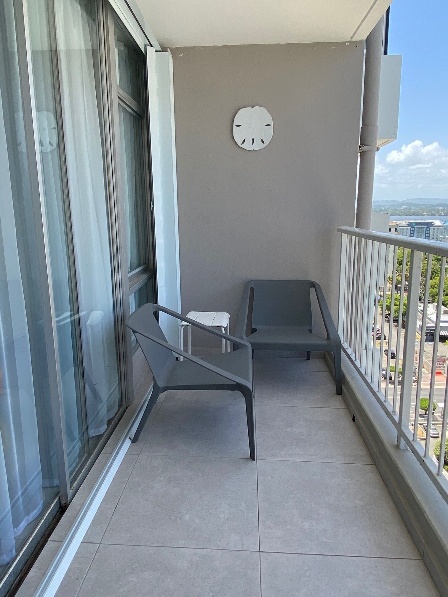 A balcony with a view of the city, a clock on the wall, and two chairs.