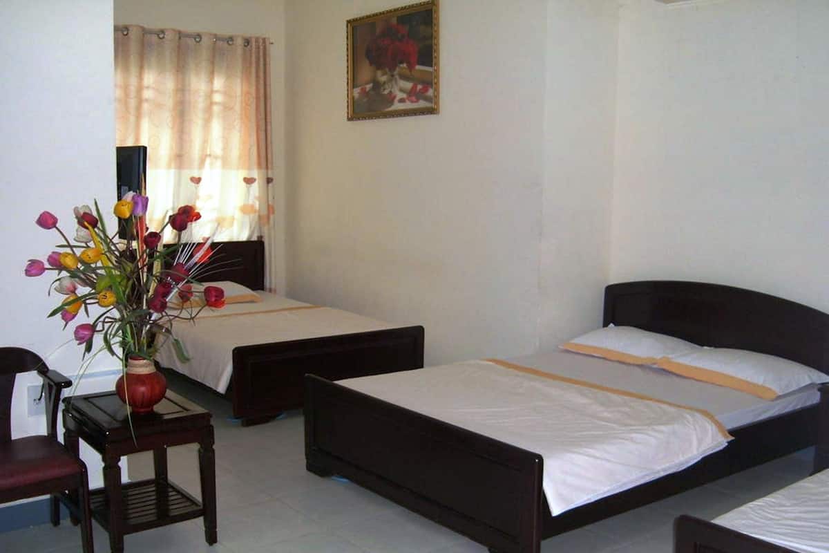 Une chambre d’hôtel avec deux lits simples, une petite table ornée d’un vase de fleurs et un tableau accroché au mur.