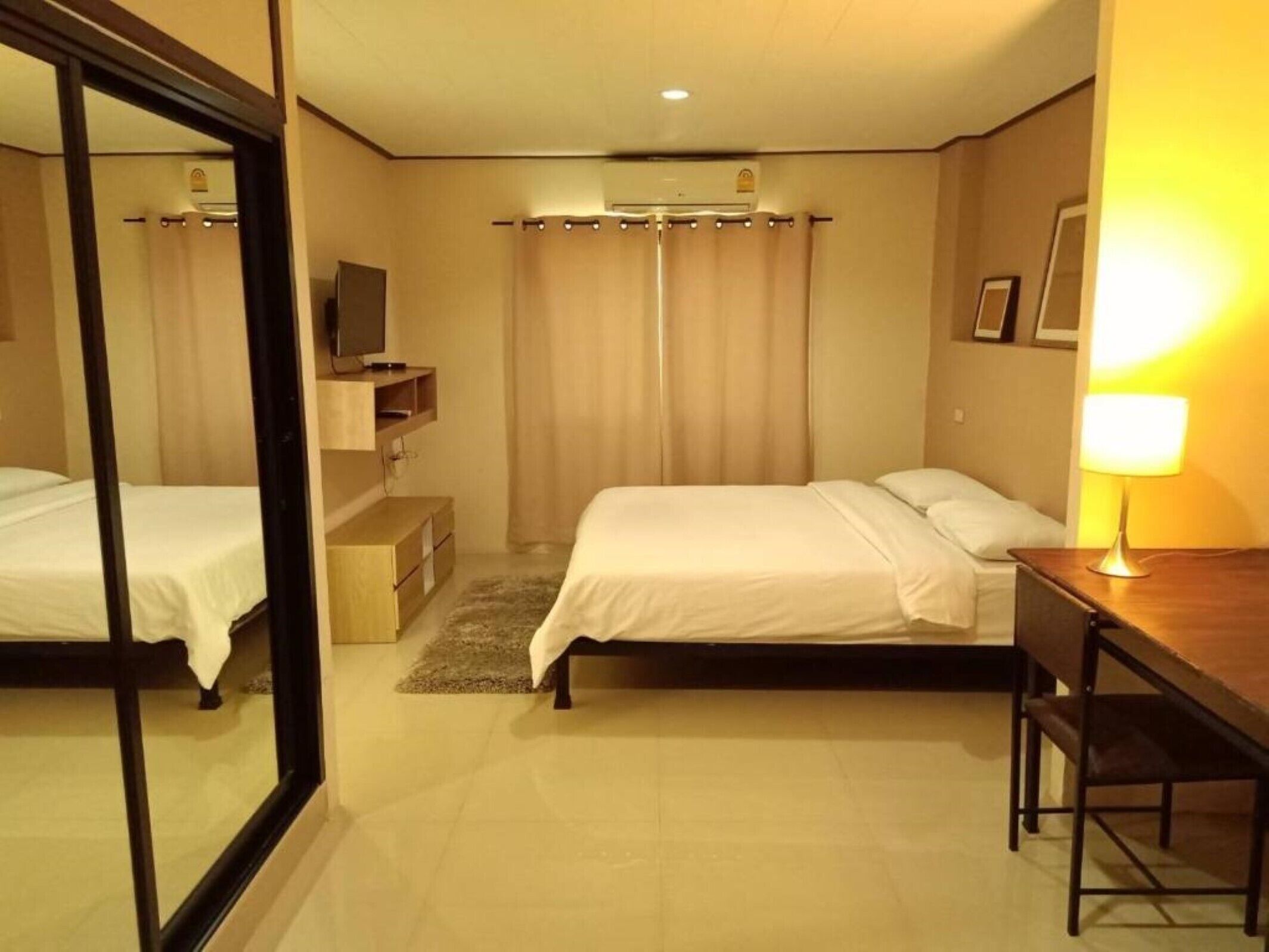 A hotel room with two beds, a desk, a TV, and a lamp.