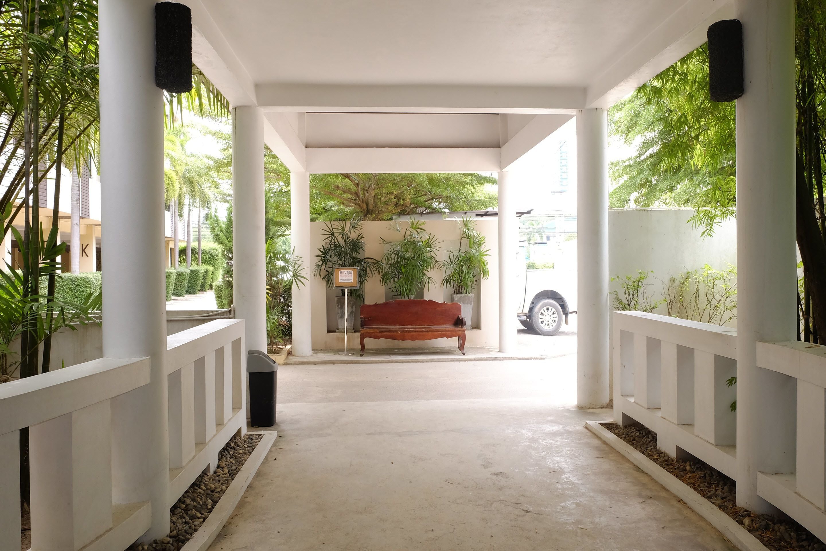 A covered walkway with white railings, a bench, and potted plants.