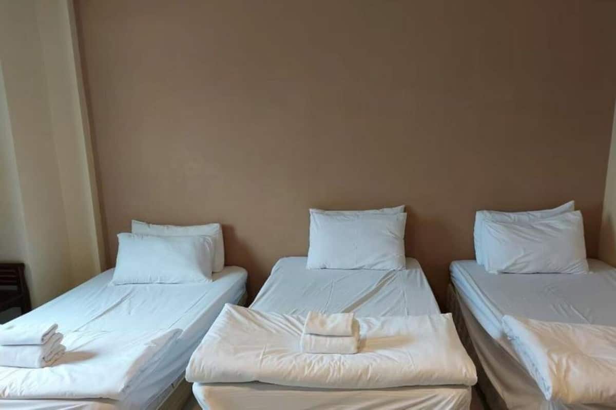 Três camas de solteiro com lençóis e almofadas brancas, dispostas em linha reta contra uma parede lisa.