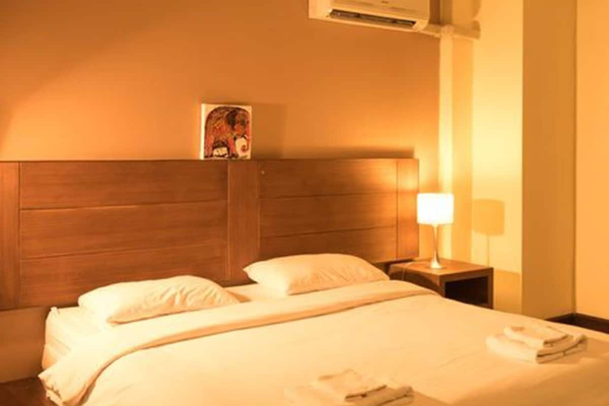 Quarto de hotel com cama de casal, mesa de cabeceira, abajur, ar condicionado e um quadro pendurado na parede.