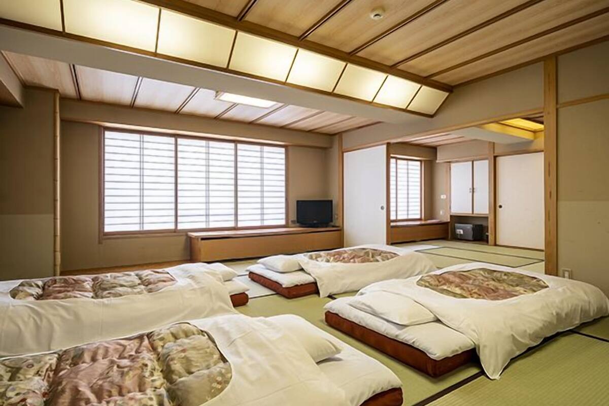 A traditional Japanese-style room with tatami flooring, multiple futons, sliding doors, and a television.