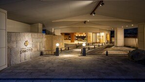 Una entrada moderna a un edificio con fachada de piedra, un logotipo y un camino bien iluminado que lleva a la entrada.