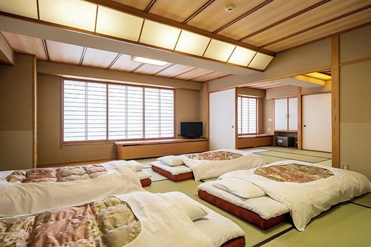 A traditional Japanese-style room with tatami flooring, multiple futons, sliding doors, and a television.