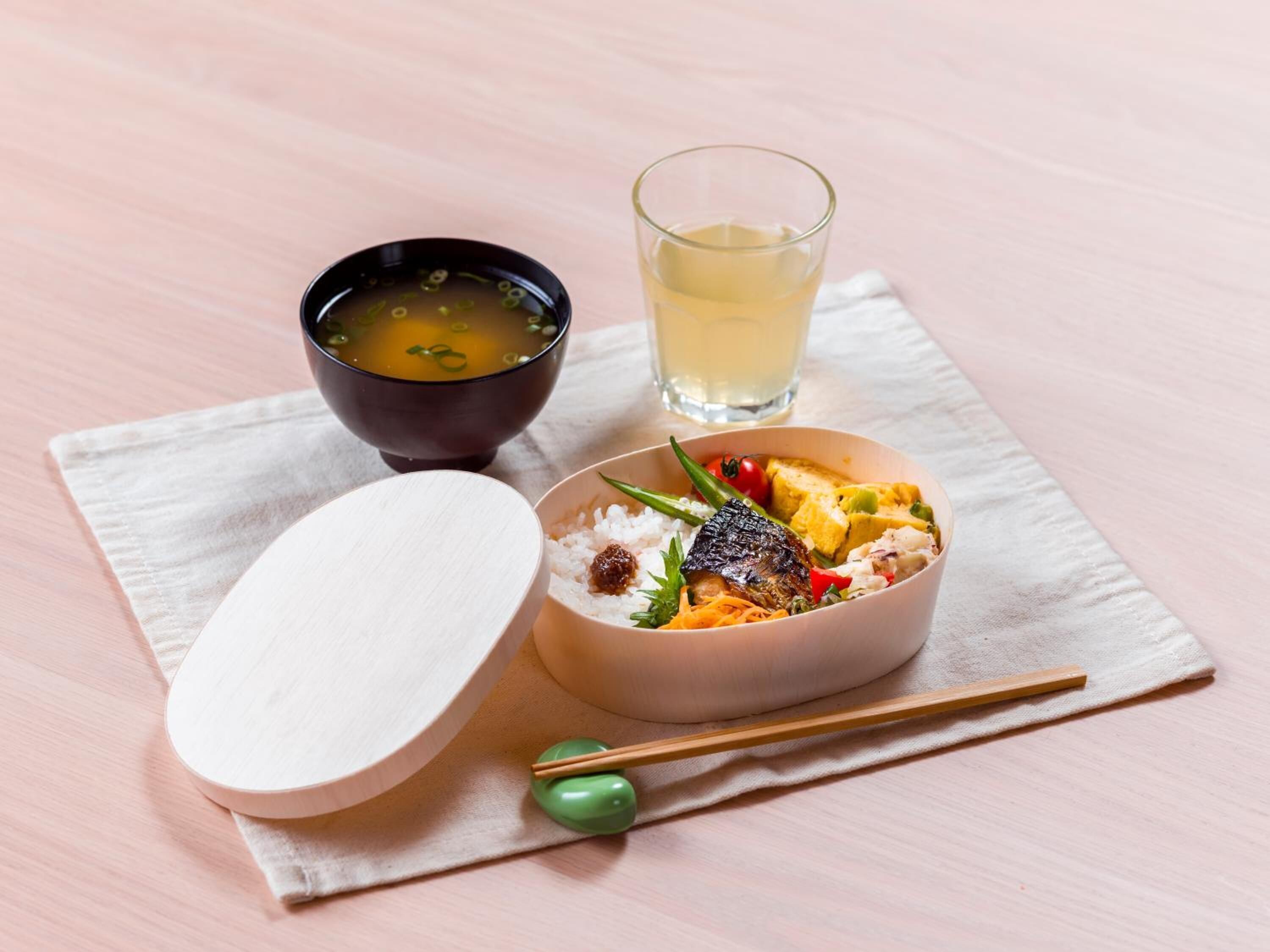 A meal with rice, vegetables, and a piece of meat, served with a soup and a glass of drink on a table.
