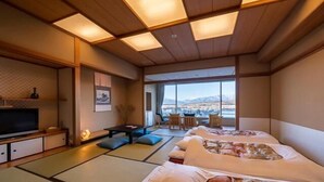 Una habitación de estilo japonés tradicional, con suelo de tatami, un futón, televisión y vistas a un paisaje montañoso.