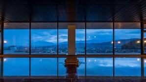 Un interior moderno con ventanas amplias que ofrecen vistas a un paisaje urbano y montañas al atardecer.