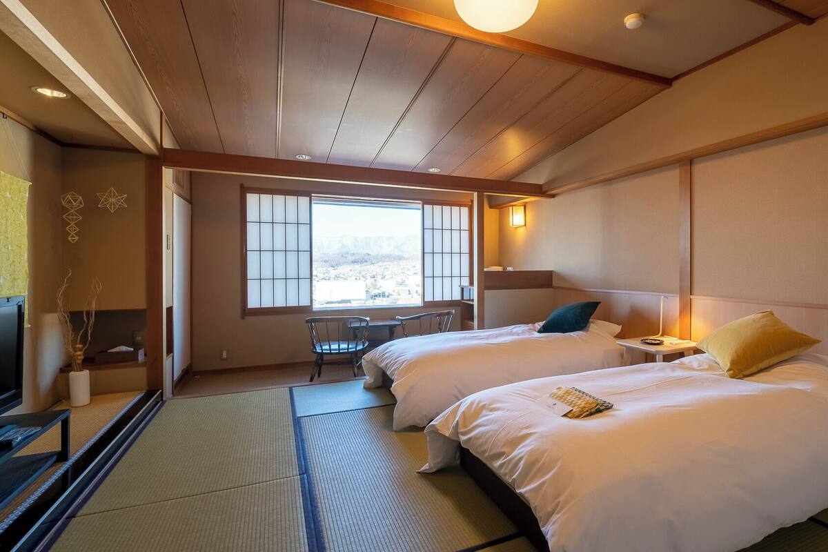 A hotel room with two beds, a desk, a chair, and a large window with a view.