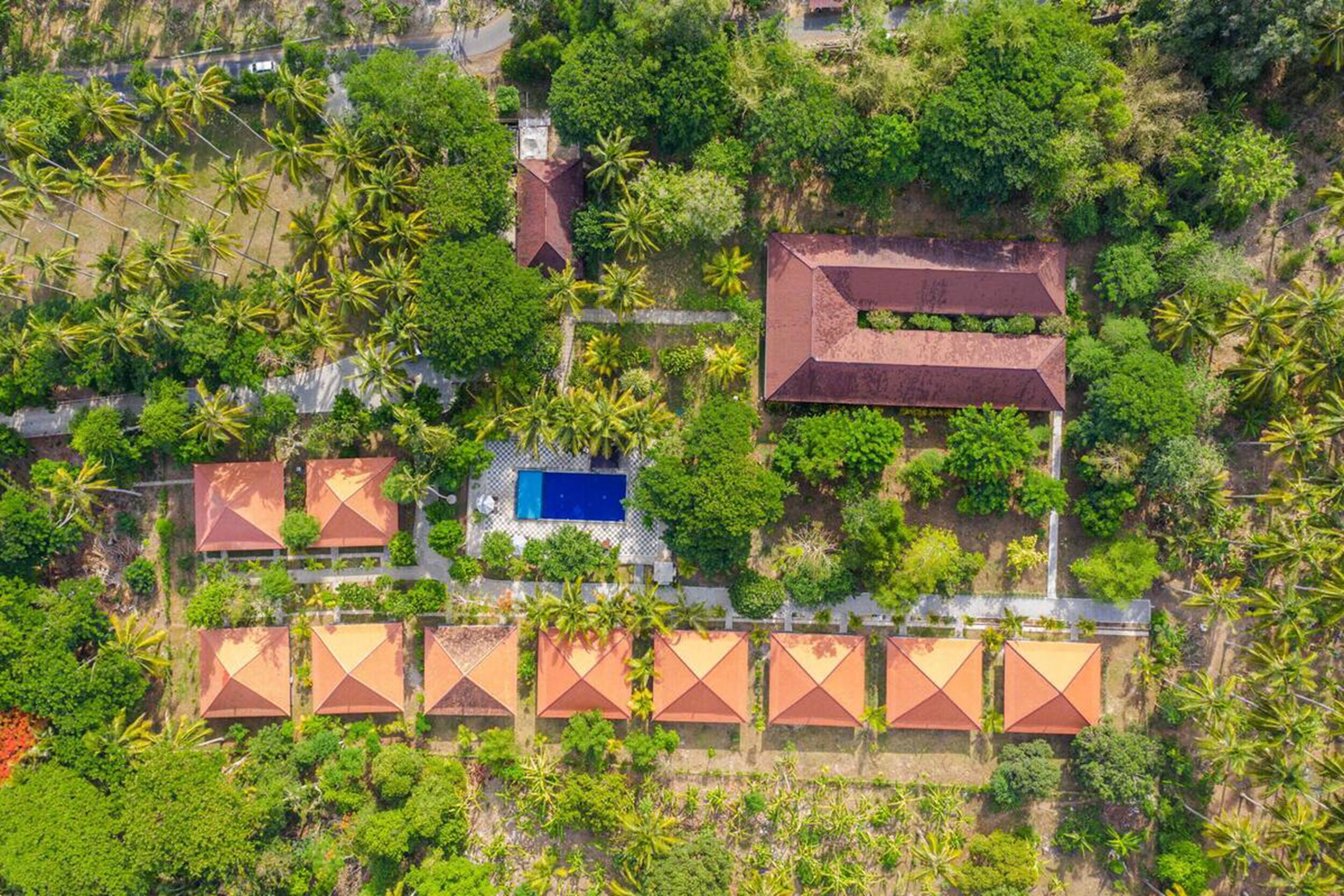 Vista aérea de um resort com vários edifícios no estilo de bangalôs, uma piscina e vegetação exuberante.