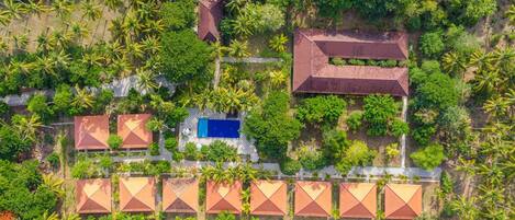 An aerial view of a resort with multiple bungalow-style buildings, a swimming pool, and lush greenery.