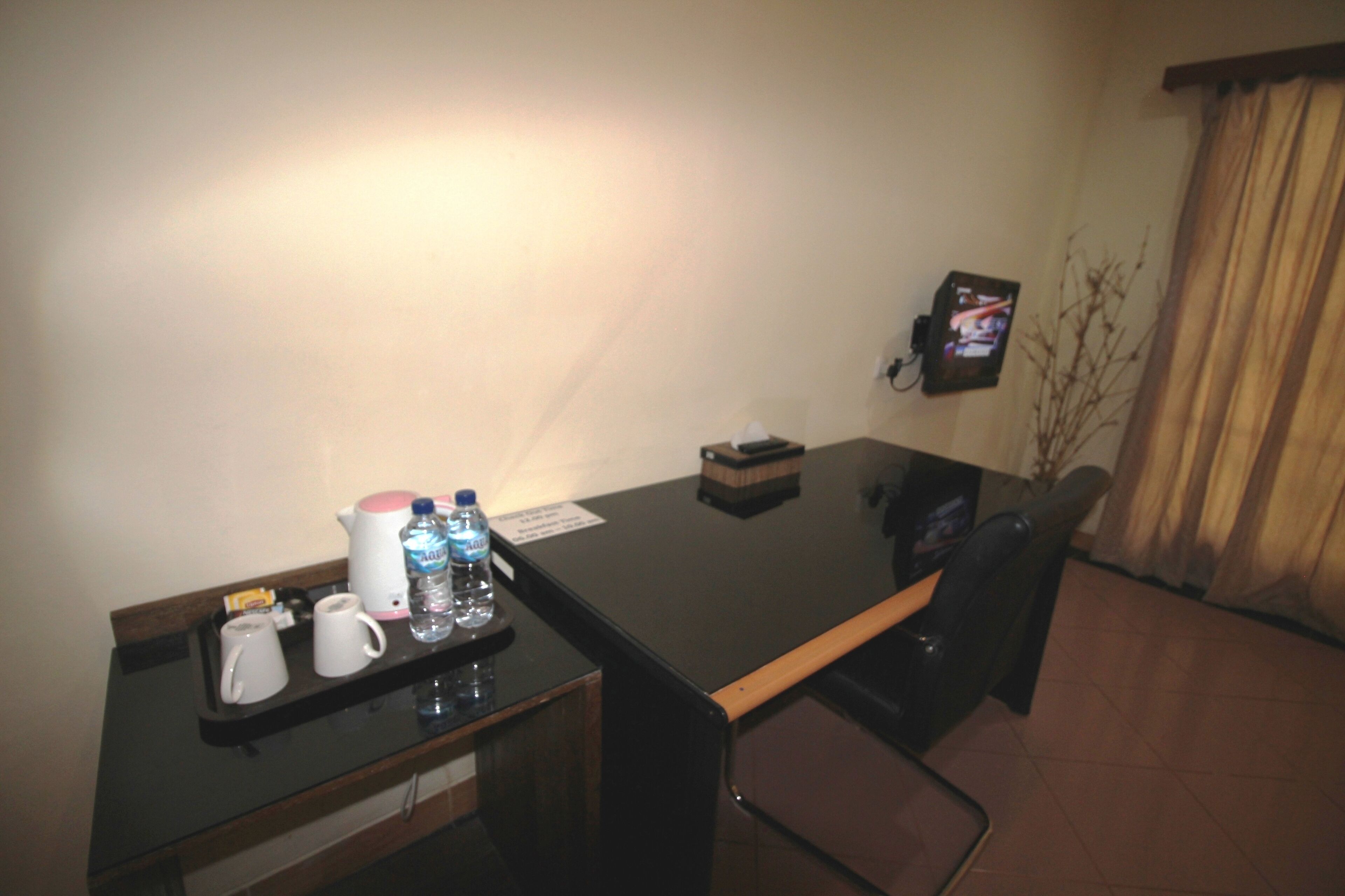A hotel room with a black desk, two white mugs, a pink coffee pot, and a water bottle.
