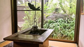 A traditional Japanese room with a tatami mat floor, a wooden table with a black kettle, and a window with a view of a garden. - Irori yado Hidaya (Takayama)