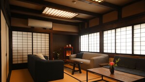 A traditional Japanese room with tatami flooring, a black sofa, a beige sofa, and a wooden table with a vase of flowers. - Irori yado Hidaya (Takayama)