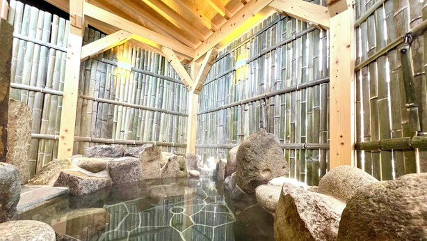 A traditional Japanese onsen with wooden beams and bamboo walls, featuring a clear hexagonal glass floor over a hot spring surrounded by rocks. - Irori yado Hidaya (Takayama)