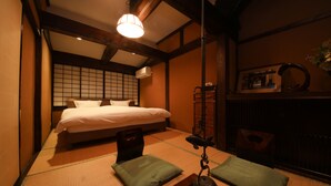 A traditional Japanese-style bedroom with tatami flooring, a bed with white bedding, a hanging lantern, and a wooden cabinet. - Irori yado Hidaya (Takayama)