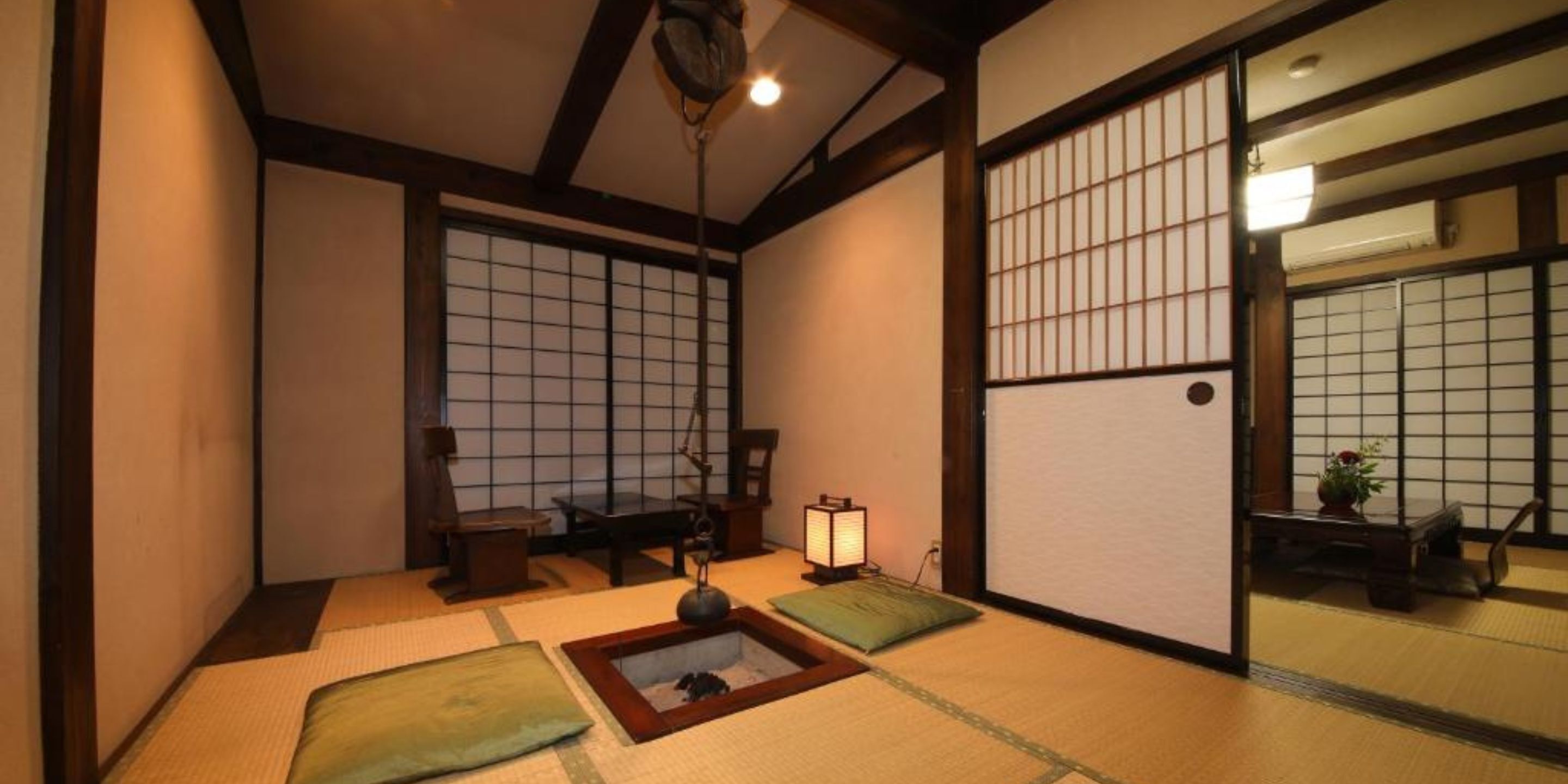 Ein traditioneller japanischer Raum mit Tatami-Boden, Shoji-Schirmen und einem niedrigen Tisch mit Kissen.