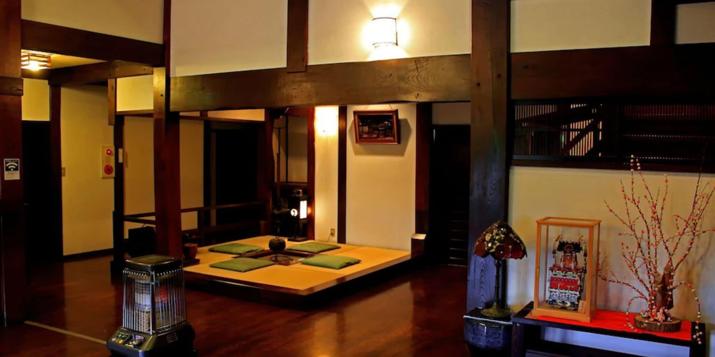 A traditional Japanese-style room with tatami flooring, a low table with cushions, a heater, and a decorative lamp.