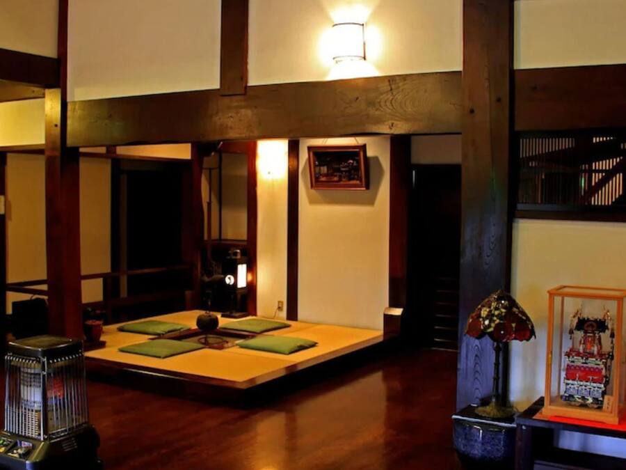 A traditional Japanese-style room with tatami flooring, a low table with cushions, a heater, and a decorative lamp.