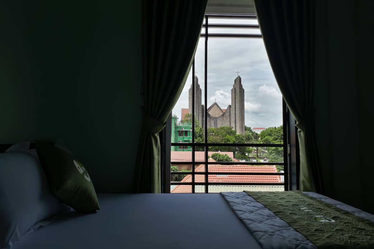 Una habitación de hotel con una cama, cortinas verdes y vistas a una iglesia con una torre alta.
