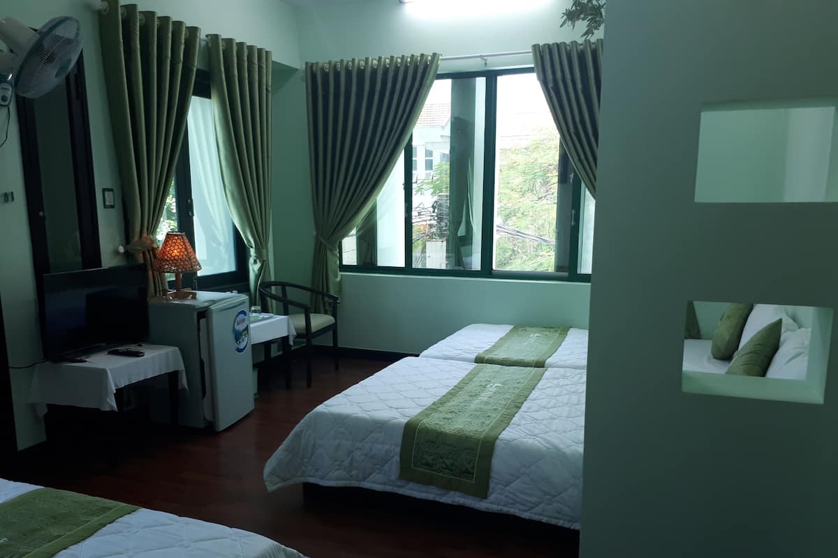 Una habitación de hotel con dos camas, un escritorio con computadora, un televisor y una ventana con cortinas.