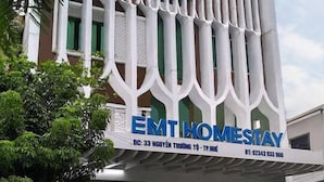 En bygning med moderne design, karakteriseret ved hvide, vertikale paneler og et skilt med teksten "EMT HOMESTAY".