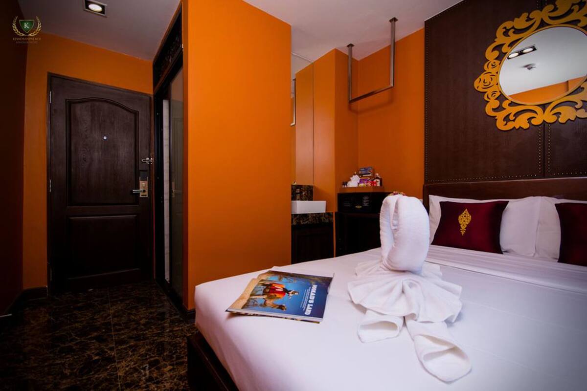 Une chambre d’hôtel avec un grand lit, une porte en bois, un miroir doté d’un cadre orné et un magazine posé sur le lit.