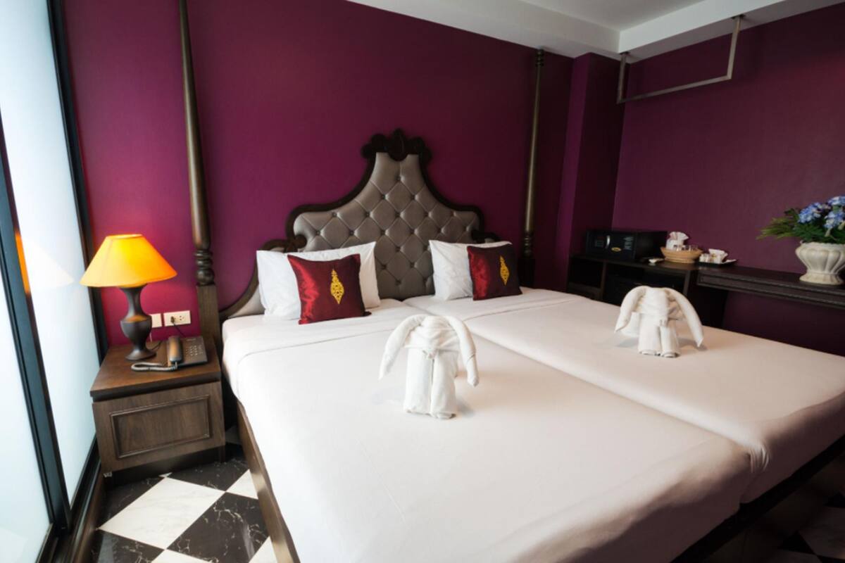 Une chambre d’hôtel avec un grand lit, deux oreillers, une table de chevet avec une lampe, un téléphone et une petite table sur laquelle est posé un vase de fleurs.