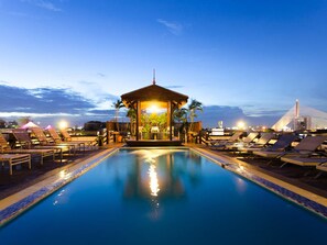 Un espace piscine avec des chaises longues et un kiosque, au crépuscule.