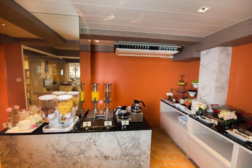 A buffet setup with various food items and beverages, a marble countertop, and a modern kitchen area with an orange wall and ceiling.