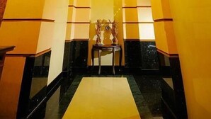 Um saguão com um lustre central, uma mesa de recepção e uma área de estar.