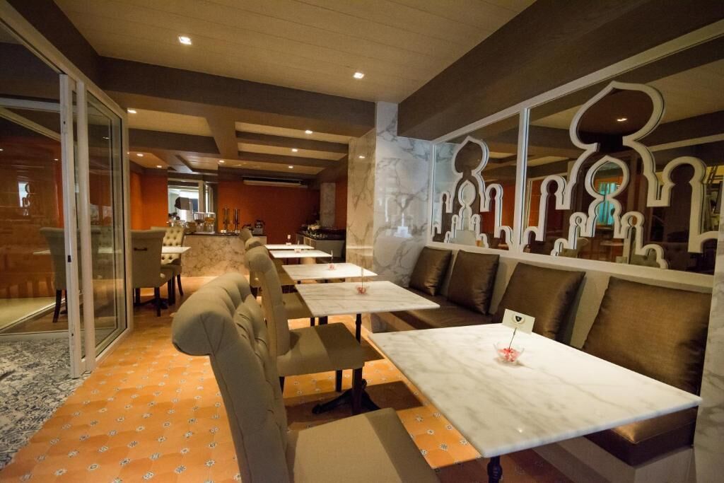 Ein Restaurant mit modernem Interieur, das eine lange Theke, Sitzgelegenheiten in Kabinen, Marmortische und einen gemusterten Teppich zeigt.