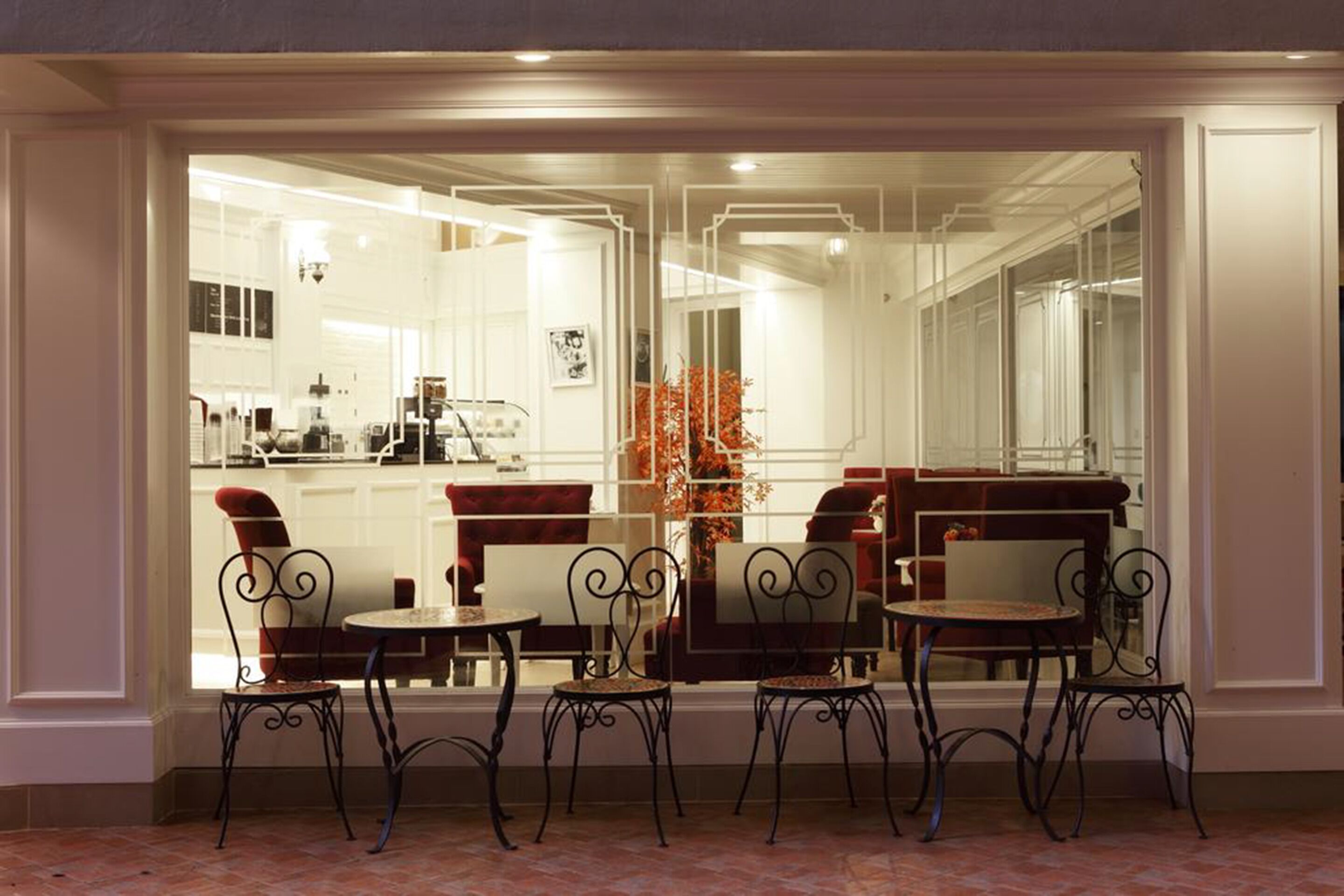 A dining area with a view of a kitchen and living space through a glass partition. There are four tables and six chairs.