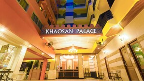 A entrada do Khaosan Palace, com um design arquitetônico moderno, exibindo uma placa de destaque e um lustre.