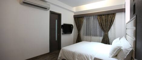 A bedroom with a bed, a ceiling fan, an air conditioning unit, a TV, and a bedside table.