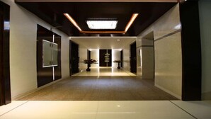 Un pasillo moderno de hotel con piso pulido, paredes oscuras y una lámpara en el centro.