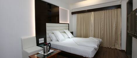 Una habitación de hotel moderna con una cama grande, una mesita de noche con hervidor, un sofá blanco y un ventilador de techo.