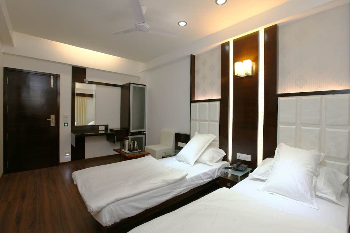 A hotel room with two beds, a ceiling fan, a bedside table with a lamp, a mirror, and a wall-mounted light fixture.