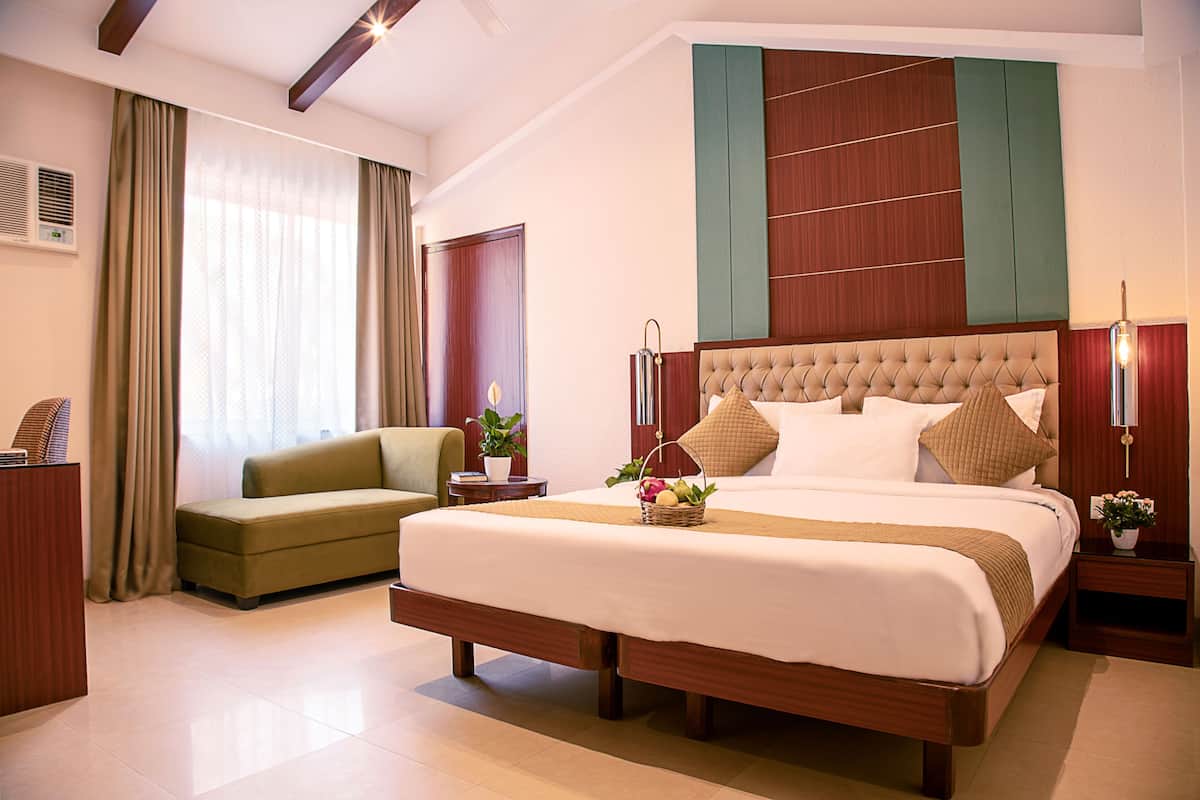 Een hotelkamer met een groot bed, een groene bank, een houten nachtkastje en een houten kledingkast.