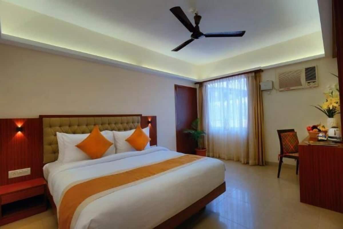 Een hotelkamer met een groot bed, een plafondventilator, een bureau en een raam met gordijnen.