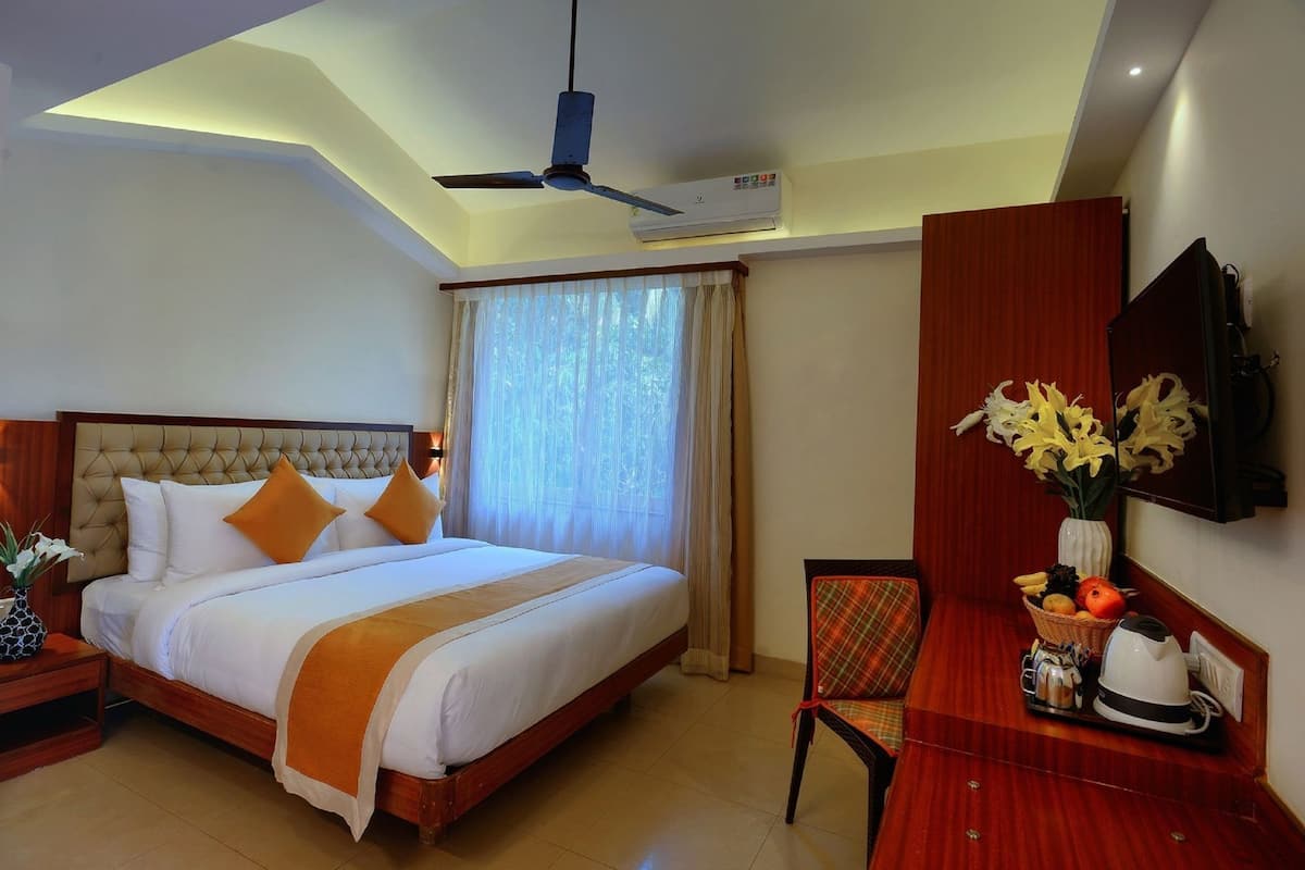 Een hotelkamer met een bed, een bureau met stoel, een plafondventilator, een airconditioning en een raam met gordijnen.
